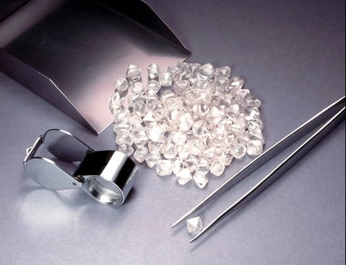 Pile of diamonds next to single diamond in tweezers and jewelers magnifier